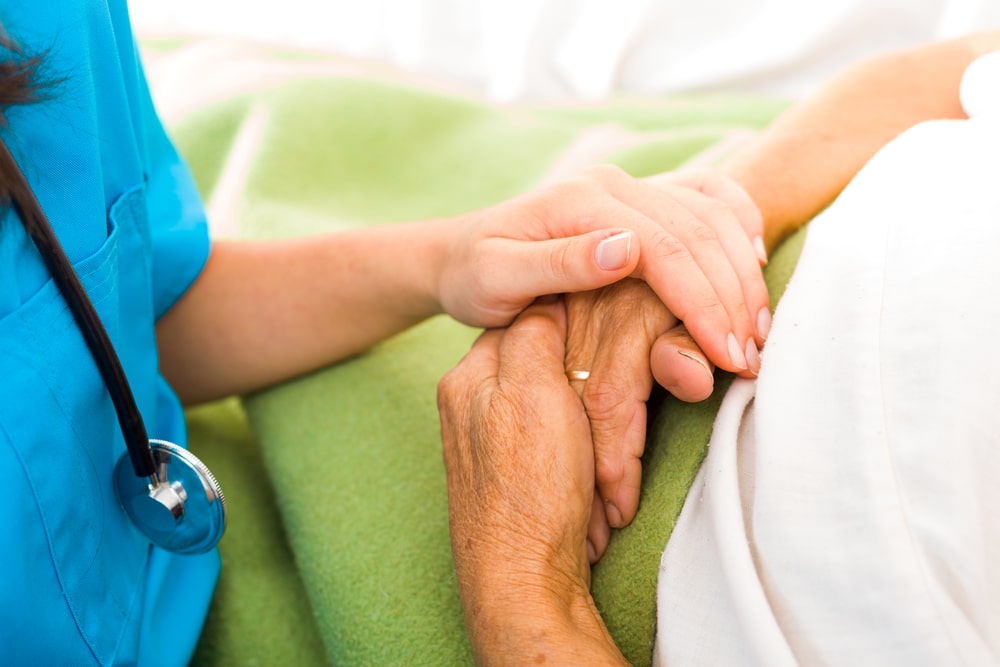 Close-up of nurse placing hand atop a senior's clasped hands