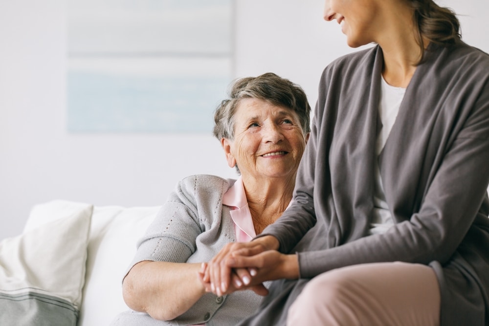 Senior woman sitting on couch, smiling at younger woman and holding her hand