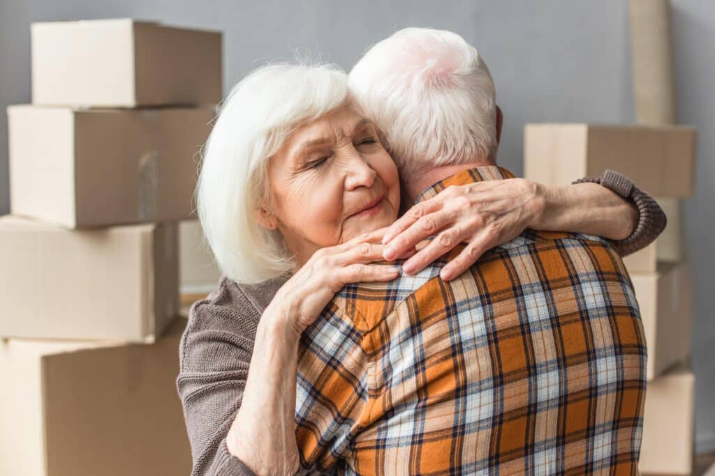 Senior couple hugging, moving boxes in background