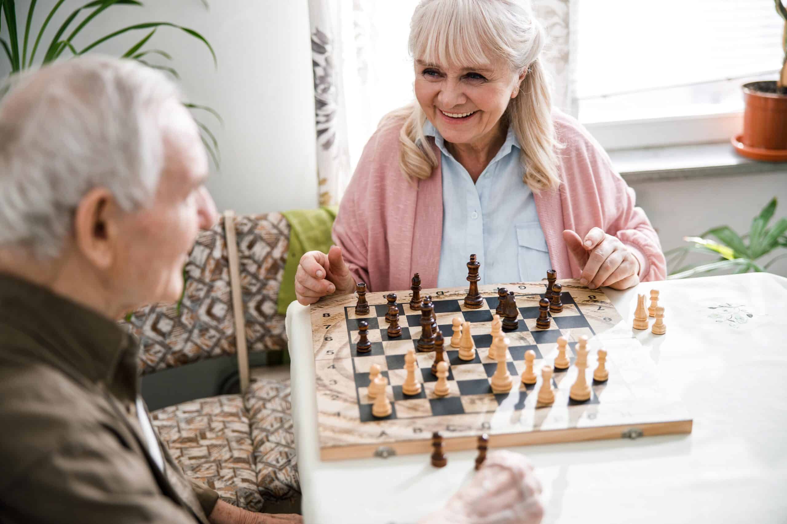 Smiling senior woman playing chess with a senior man