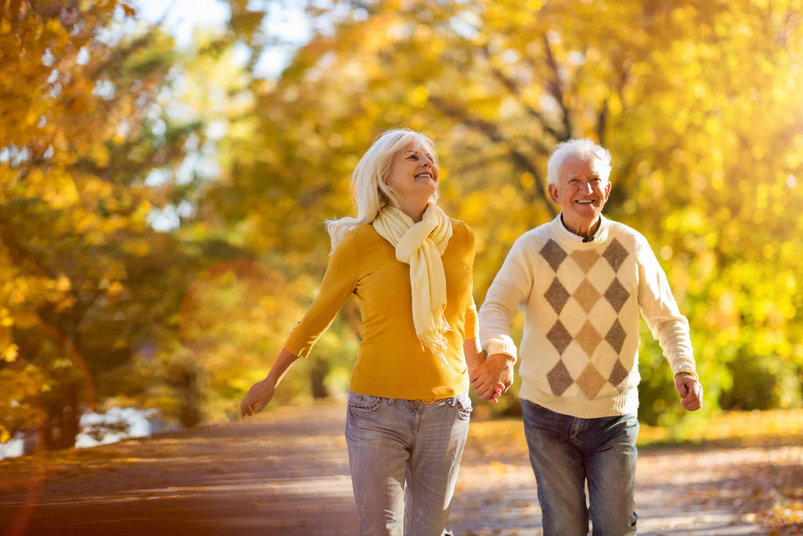 Senior couple holding hands and smiling outside in beautiful autumn leaves